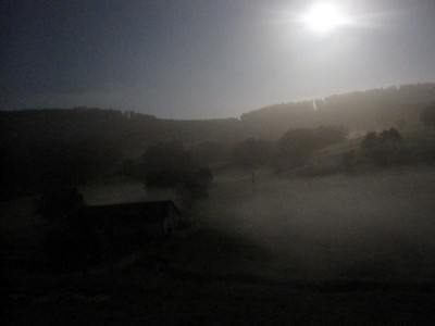 A barn in the Swiss Jura in the dark and at night, lit by a full moon.